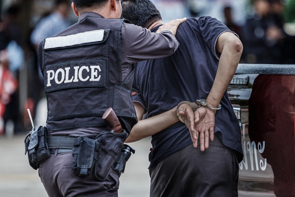Police officer guiding a handcuffed person toward a vehicle during an arrest.